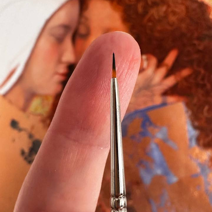 Close-up of a brush held between fingers with a blurred painting in the background