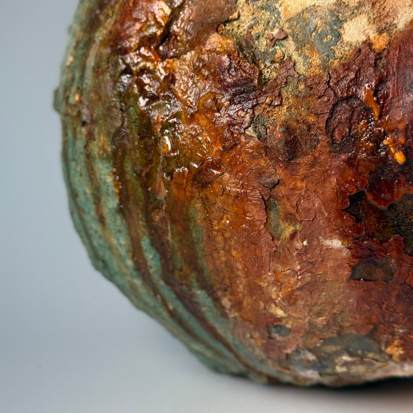 Close-up of rustic ceramic vase with green and brown patina on a gray background