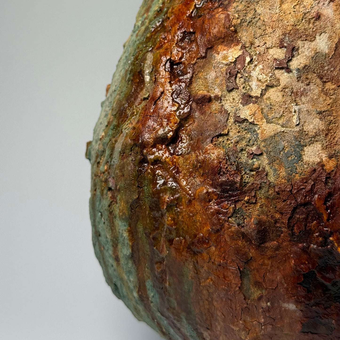 Close-up of rustic ceramic vase with green and brown patina on a gray background