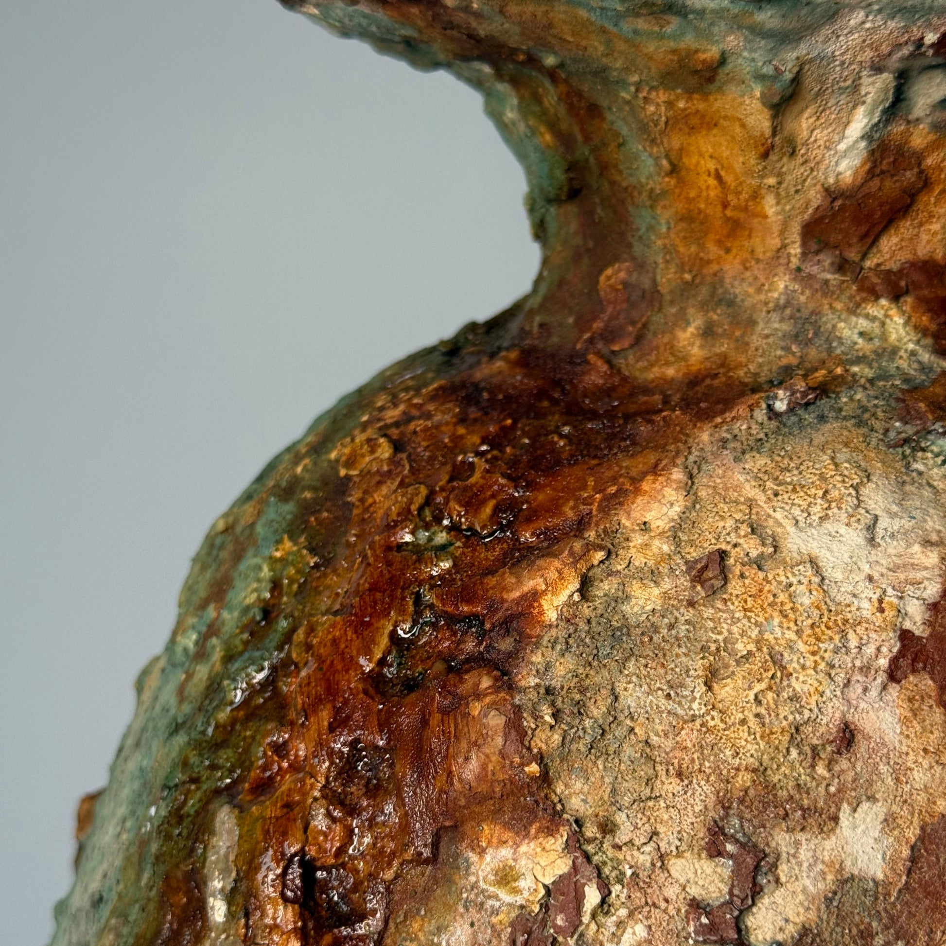 Close-up of rustic ceramic vase with green and brown patina on a gray background