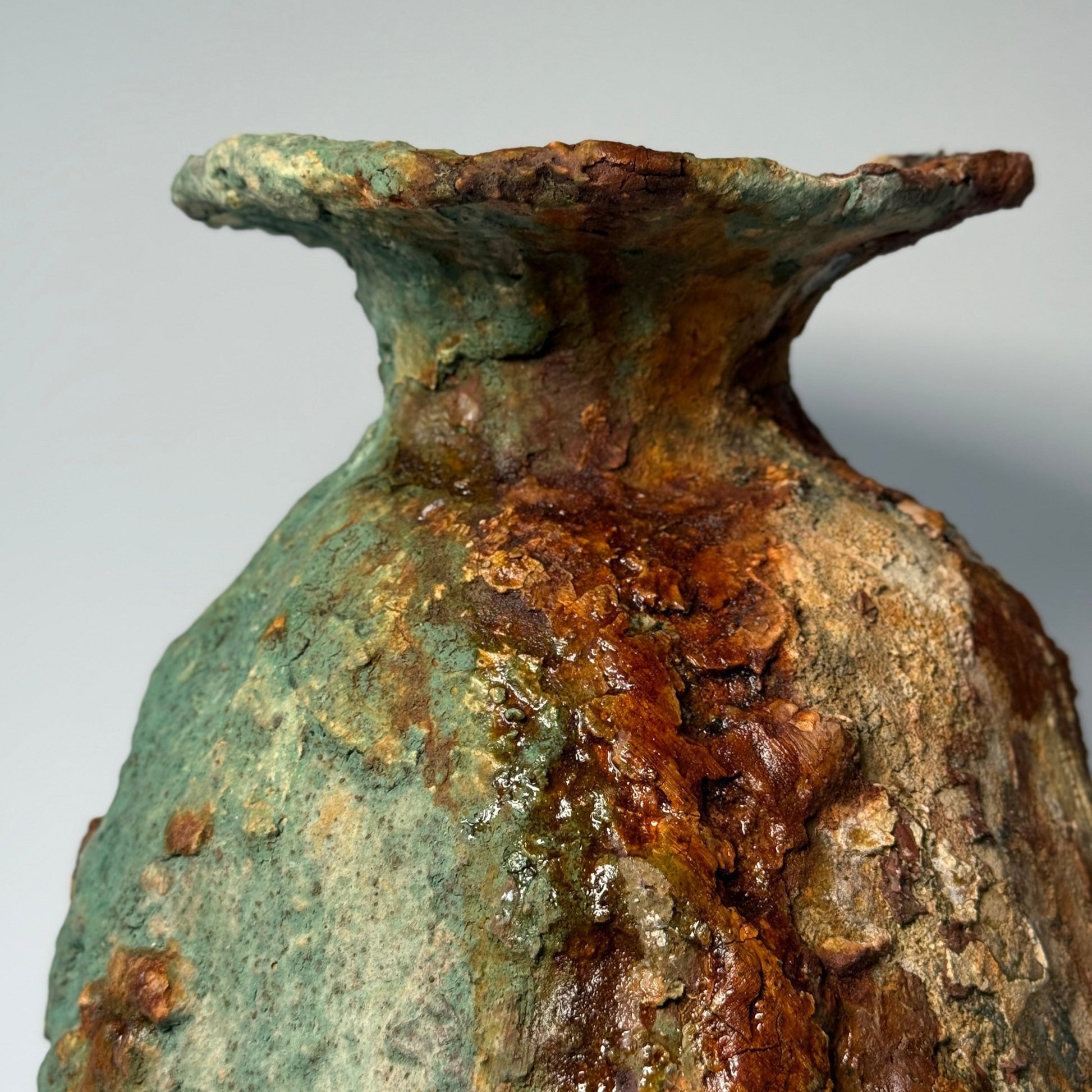 Close-up of rustic ceramic vase with green and brown patina on a gray background