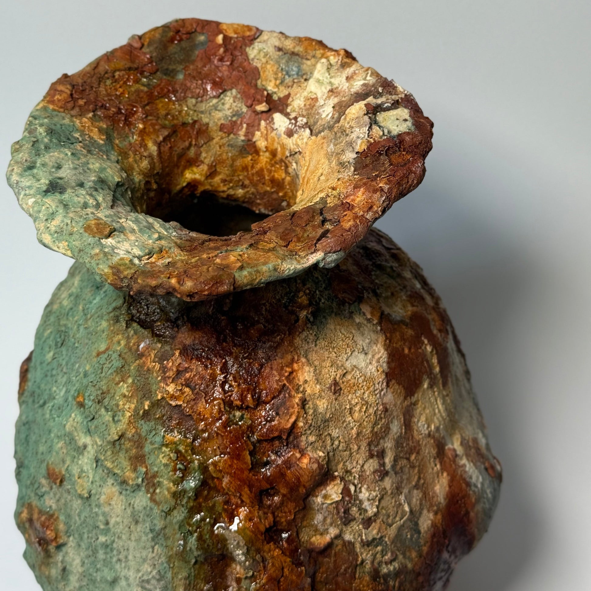Close-up of rustic ceramic vase with green and brown patina on a gray background