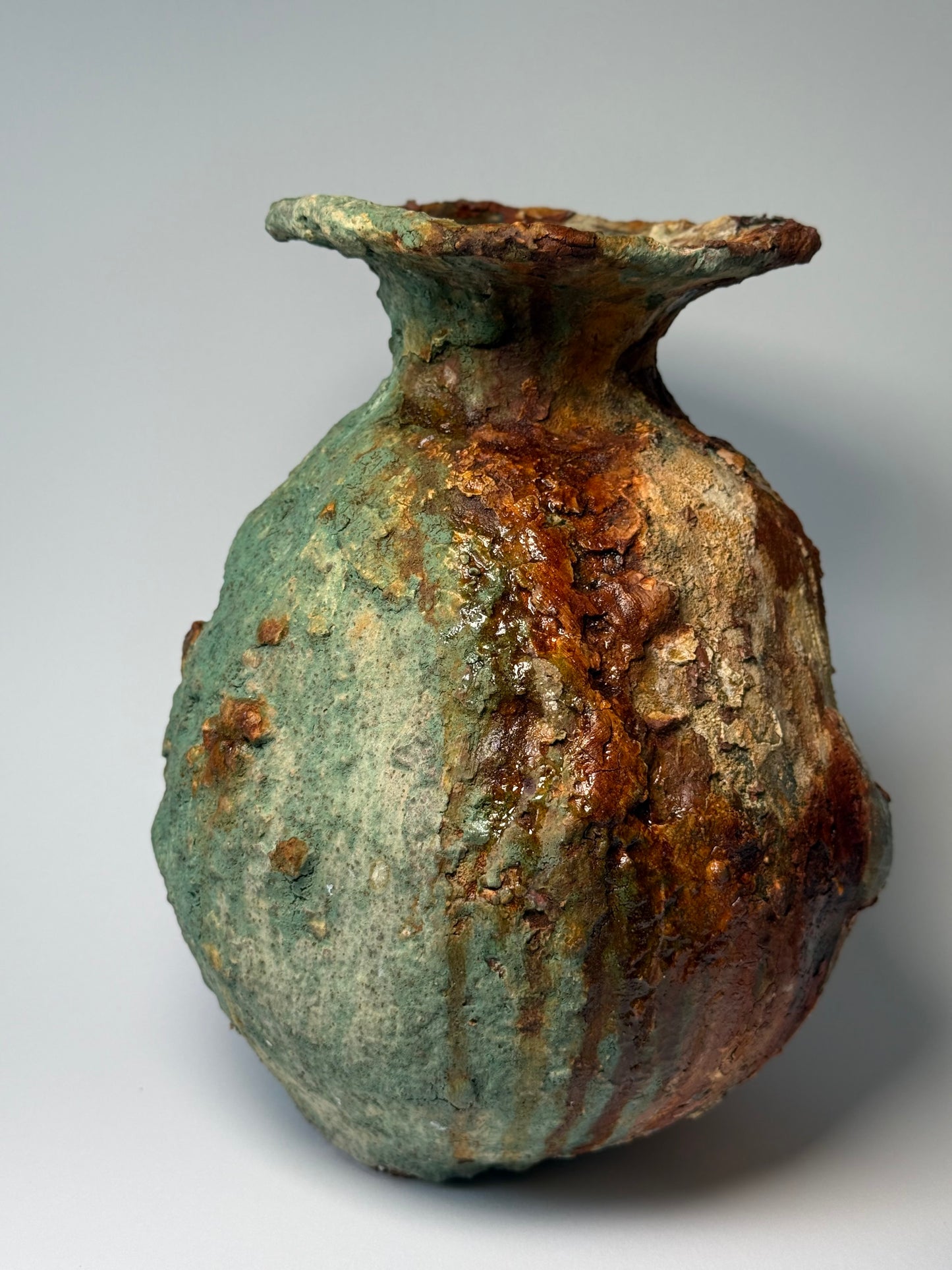 Rustic ceramic vase with green and brown patina on a gray background