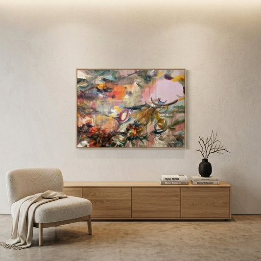 An abstract painting with a mix of pink, orange, green, and blue tones is displayed on a white wall in a modern, minimalist living room with a light wood console table, a beige armchair, and a black vase.