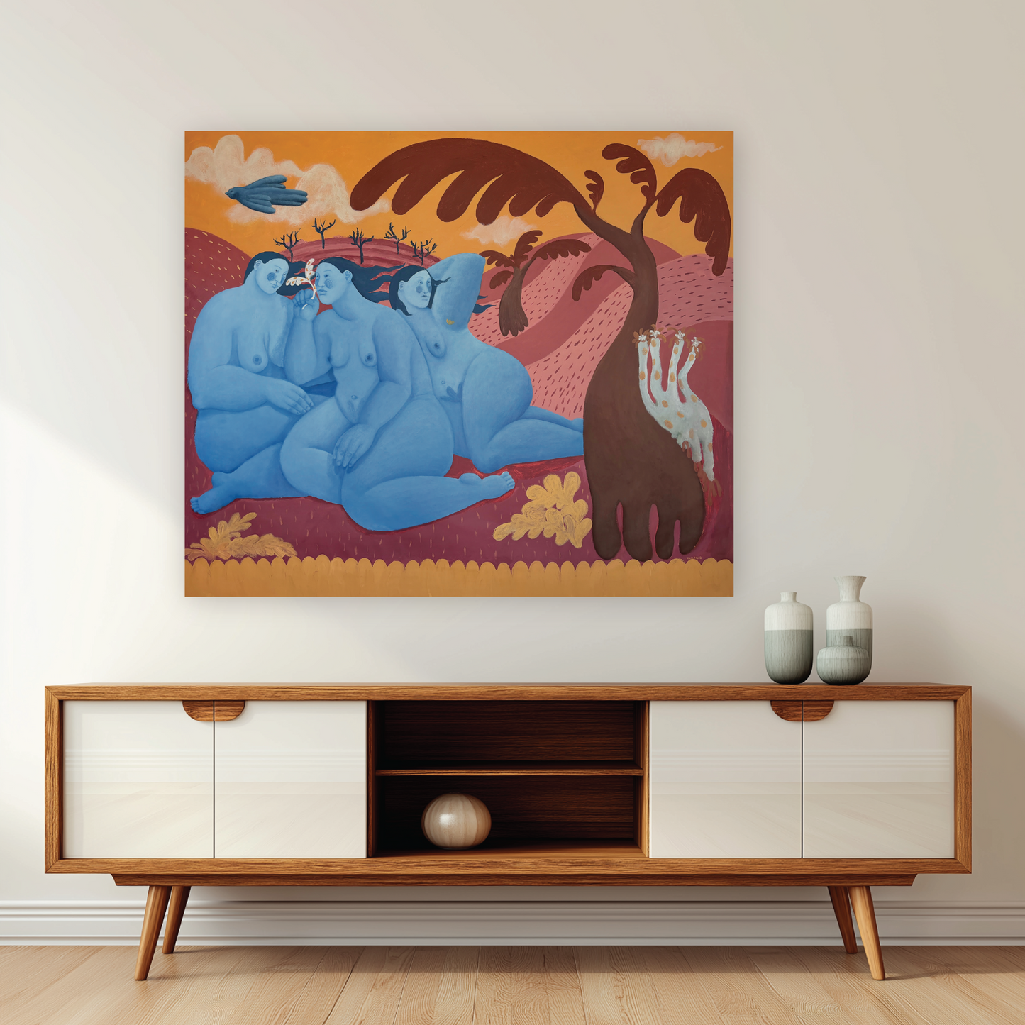 Artwork of three blue figures in a naive desert landscape above a wooden cabinet.